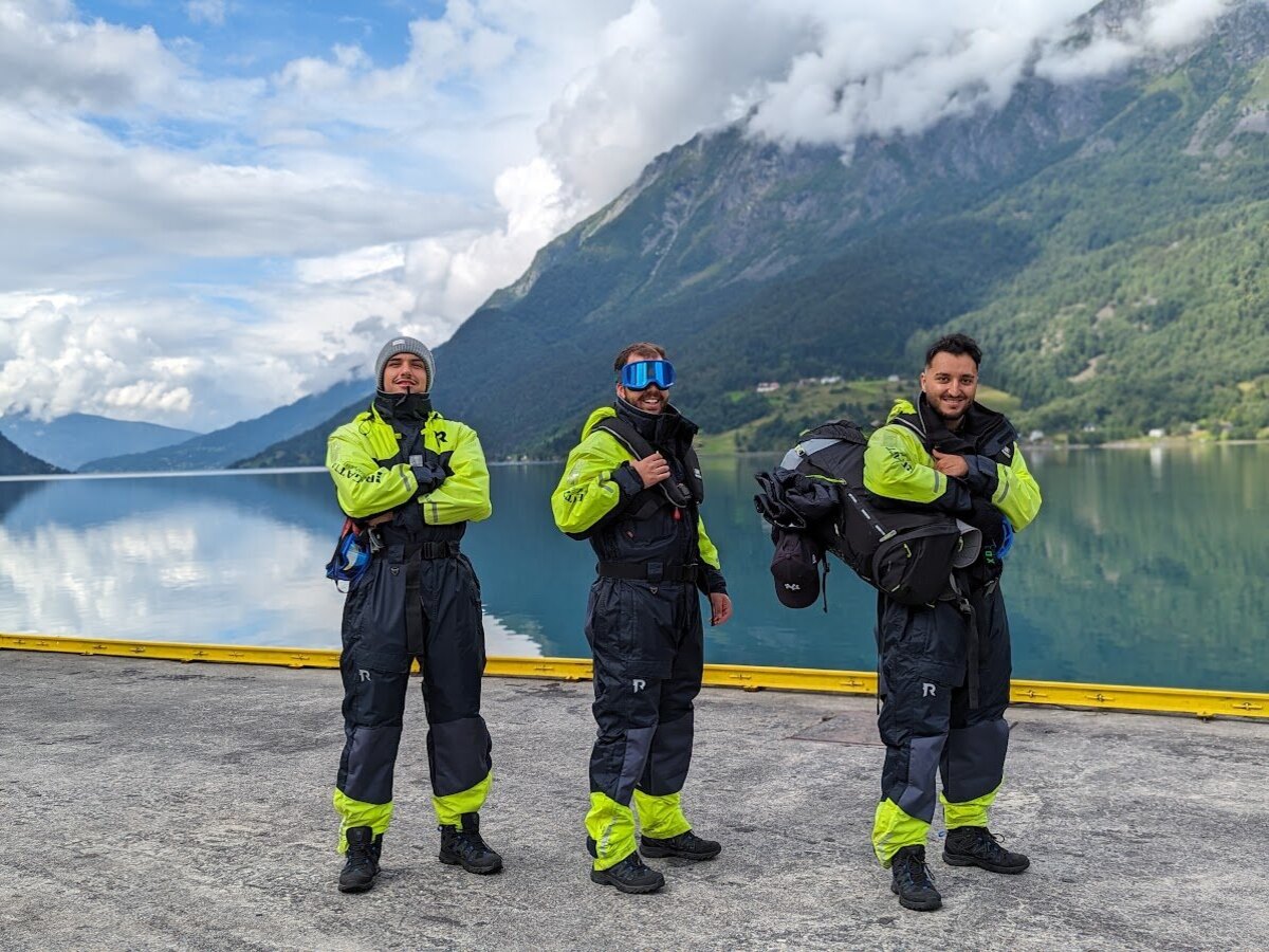 Three travellers suited up in yellow and navy fjord flotation suits on the waterfront