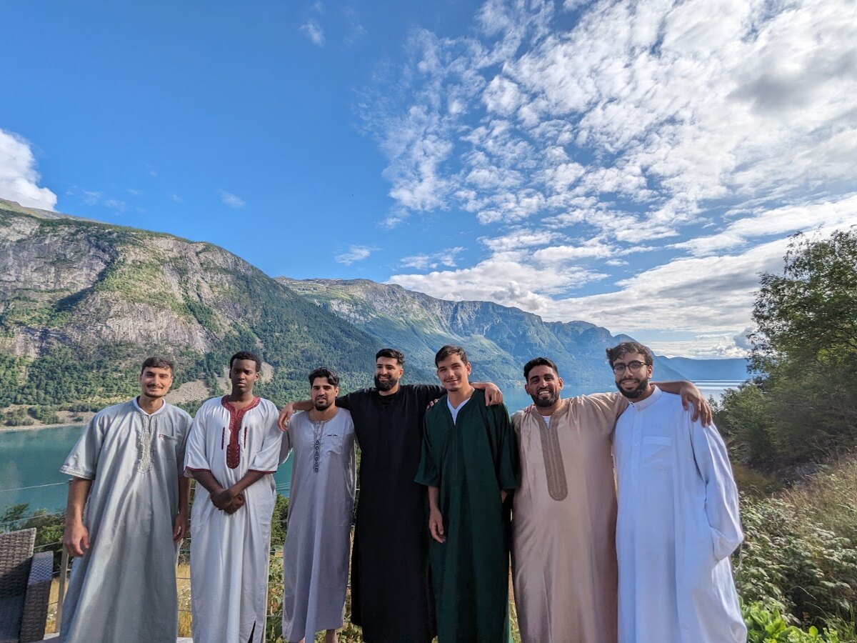 Hosted guests in traditional attire smiling together on a mountain terrace above the fjord