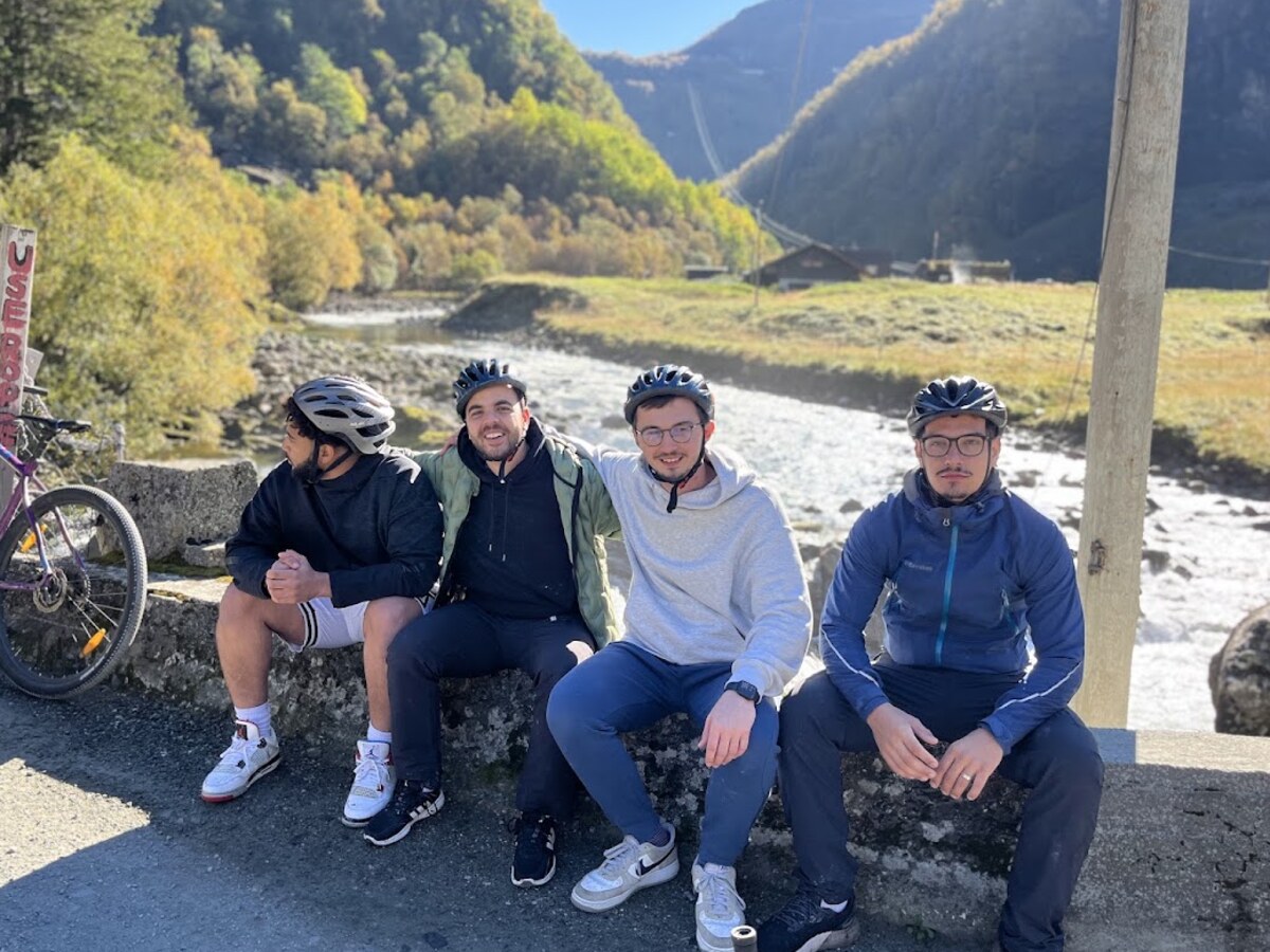 Four cyclists resting on a stone wall beside the sunny glacial river in Flåm valley