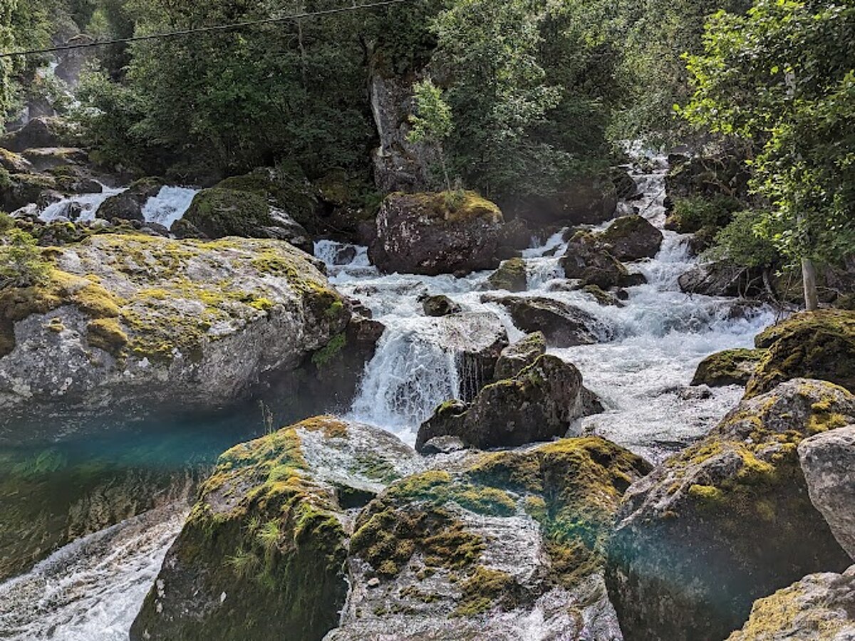 Crystal-clear glacial rapids rushing over mossy boulders in a Norwegian mountain valley