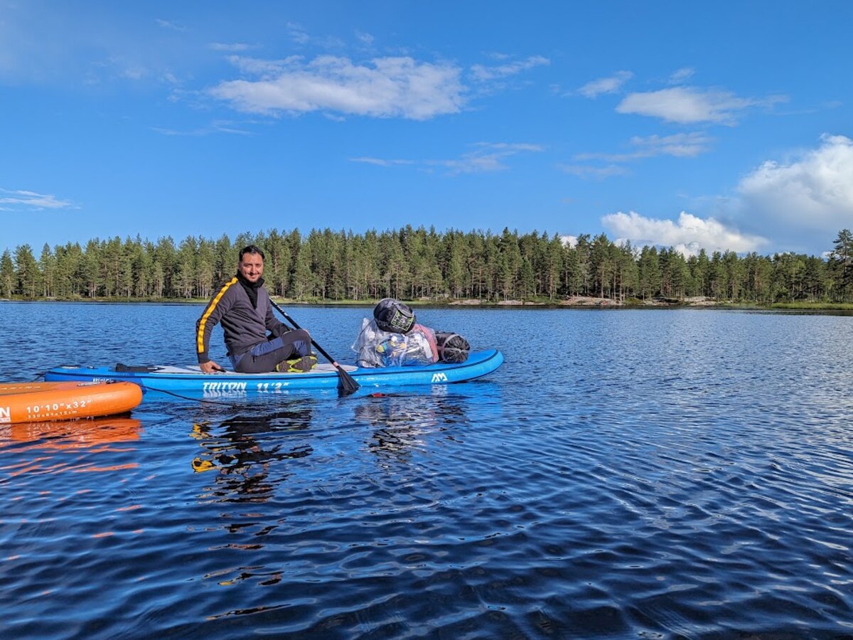 Paddleboarding on a calm pine-ringed lake in Norway under a blue summer sky